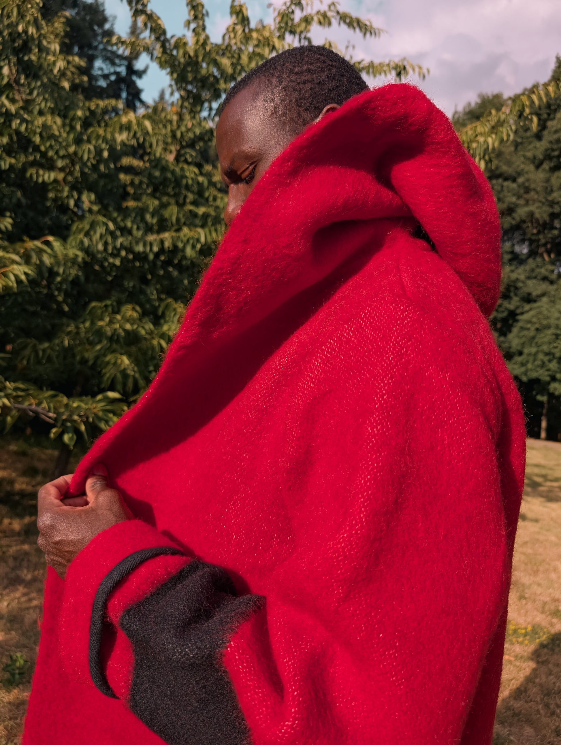 Closeup of a thick red wool robe coat with stripes, with the hood on extending into a shawl collar.