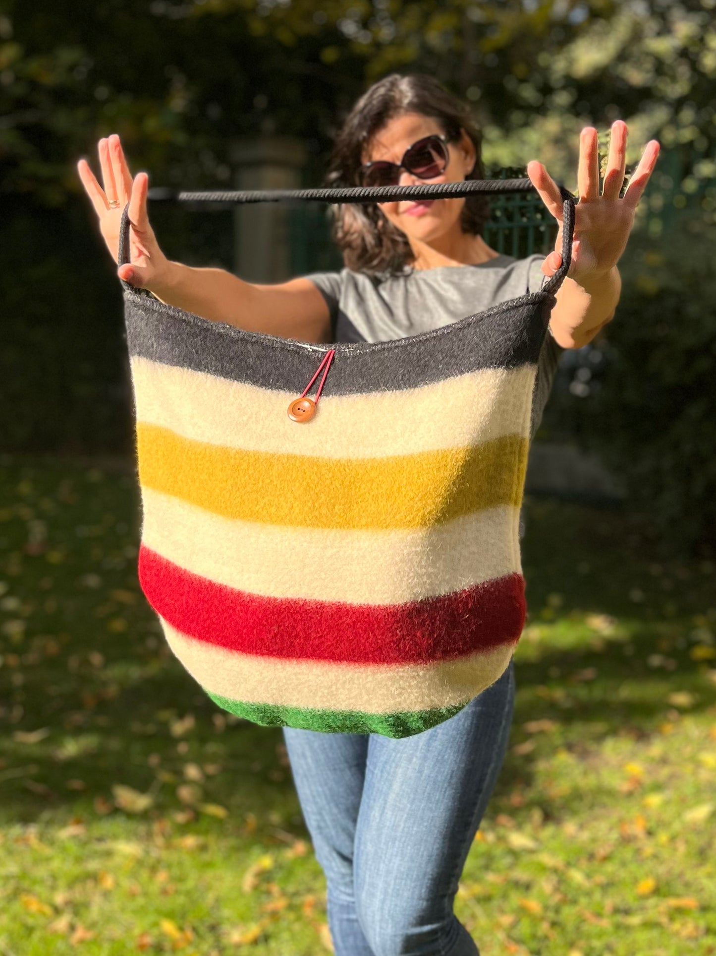 Woman holding a fashionable striped bag with colorful traditional lines and a black cotton rope strap. The bag is wide and functional, handmade from a wool blanket.