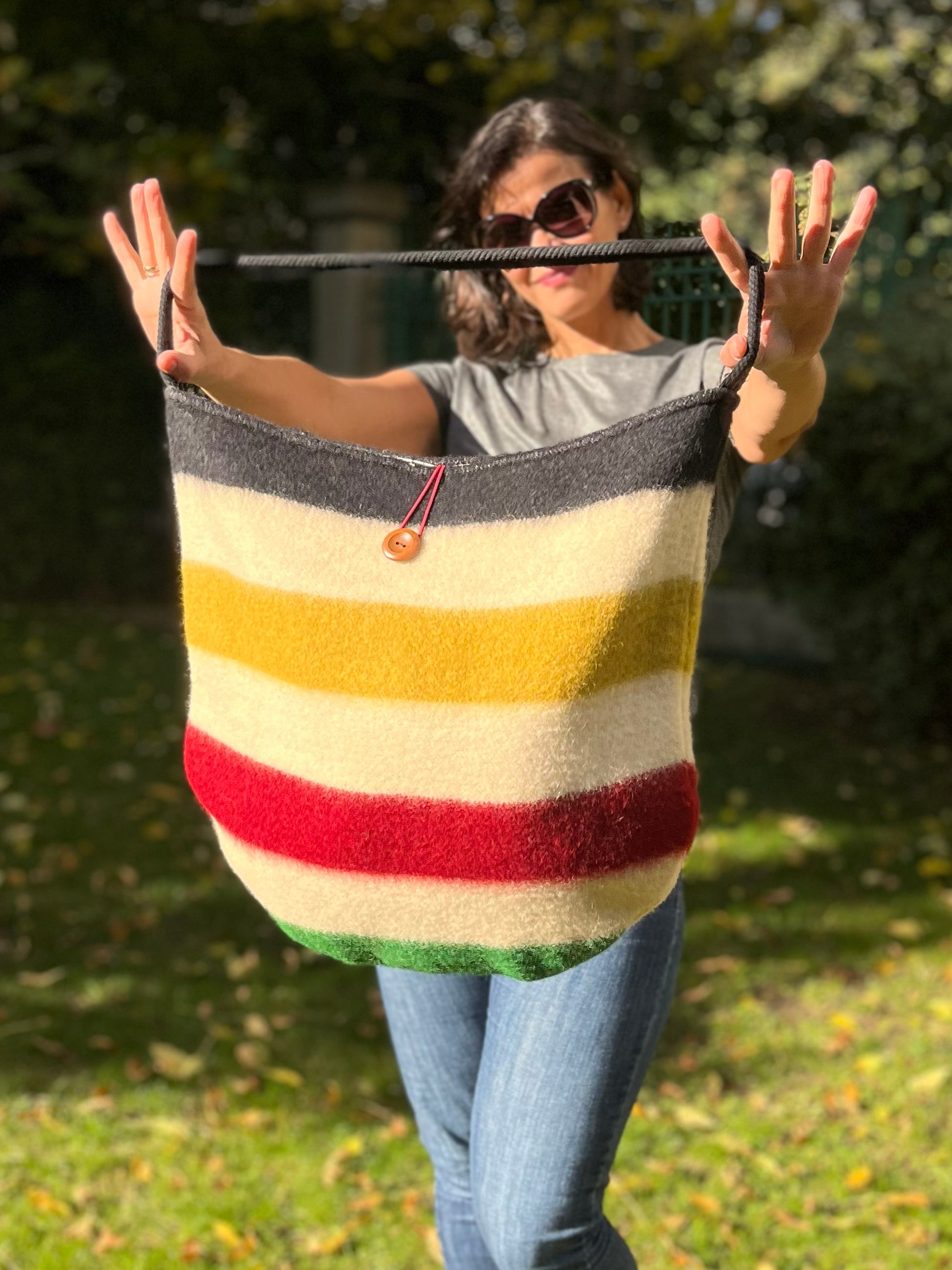 Woman holding a fashionable striped bag with colorful traditional lines and a black cotton rope strap. The bag is wide and functional, handmade from a wool blanket.
