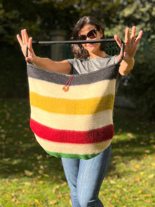 Woman holding a fashionable striped bag with colorful traditional lines and a black cotton rope strap. The bag is wide and functional, handmade from a wool blanket.