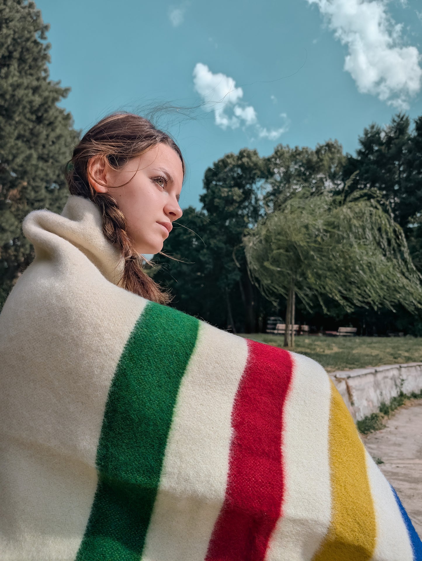Closeup of a girl wrapped in a multi stripes wool  blanket with trees and skies in the background