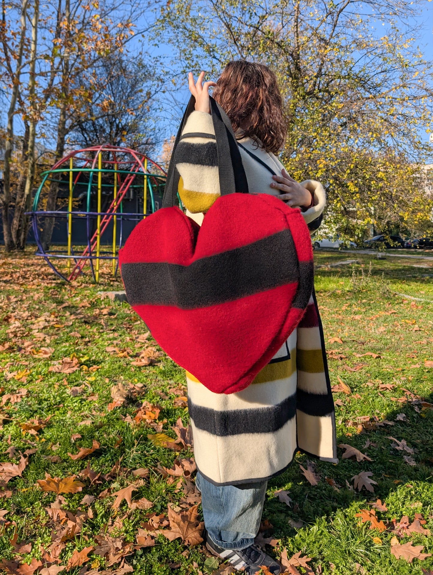 Young woman wearing an upcycled stylish striped coat and a red heart shaped tote bag in an outdoor setting.