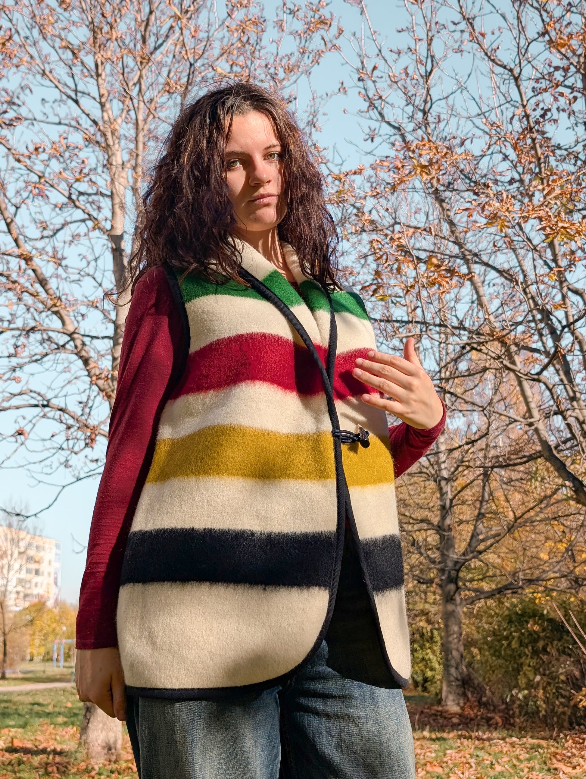 Woman wearing a unisex wool blanket vest in cream ivory base and with colorful iconic stripes. Upcycled garment.