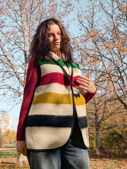 Woman wearing a unisex wool blanket vest in cream ivory base and with colorful iconic stripes. Upcycled garment.