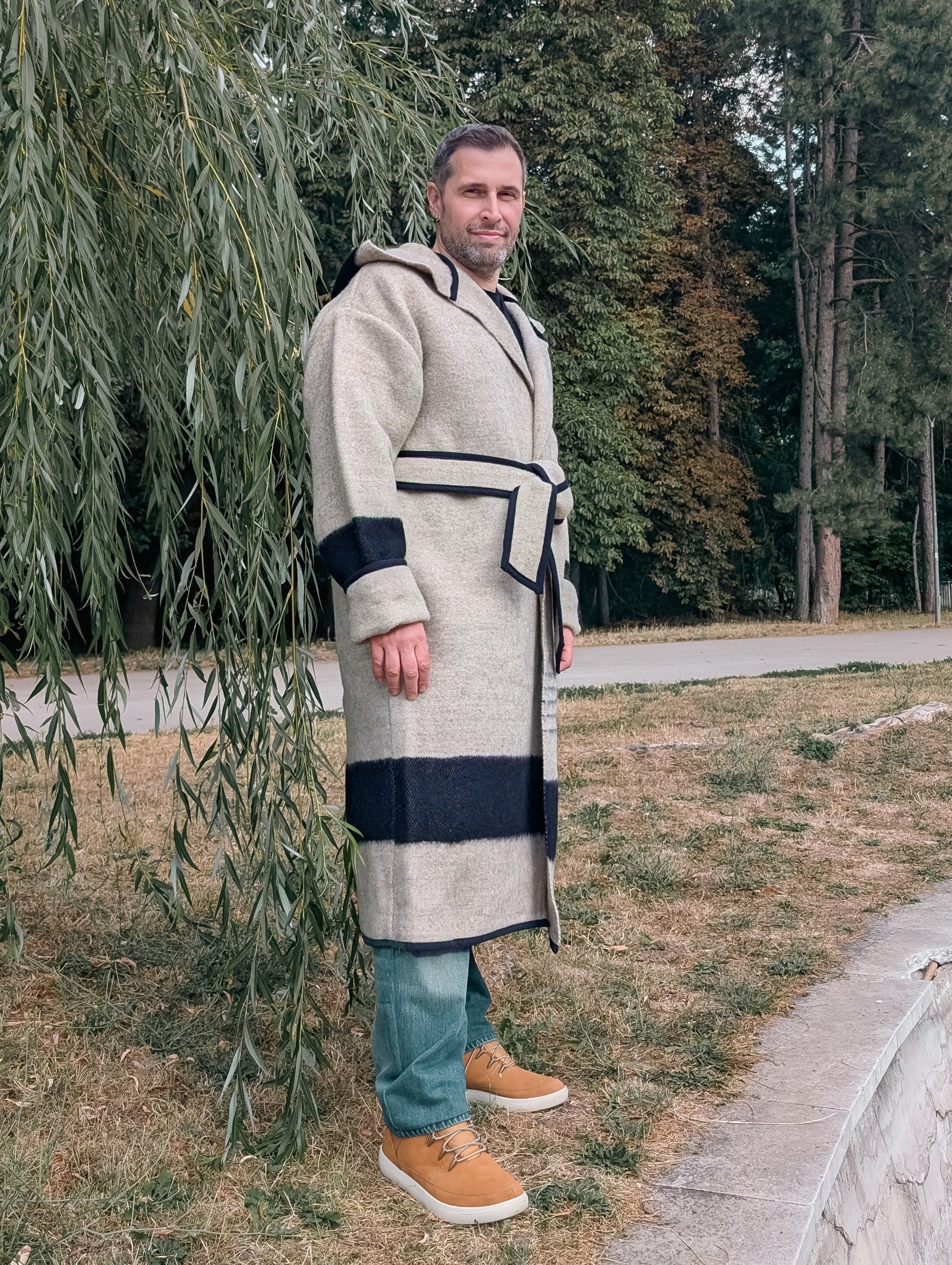 A man wearing a natural gray wool blanket capote coat with a belt.