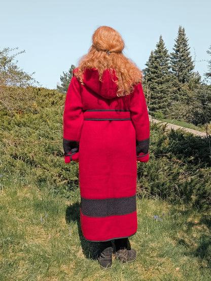 A woman posing backwards with a custom made long wool jacket in red with black stripes, hood and belt.