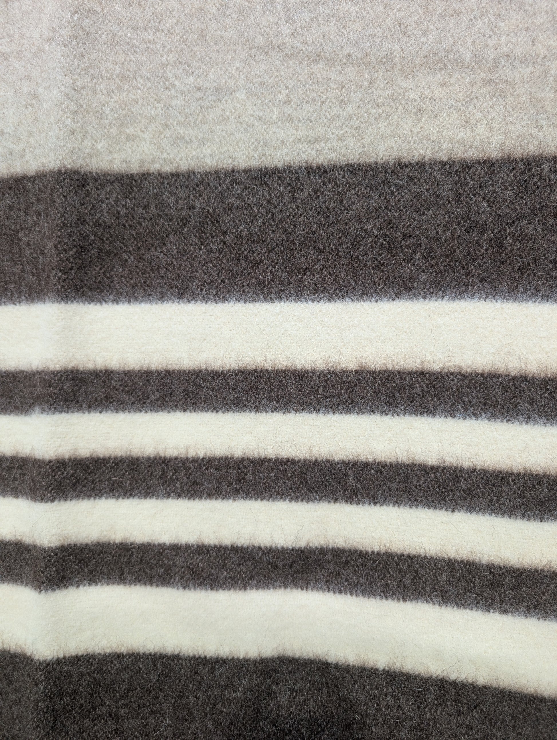 A detail of a minimalist gray wool blanket with beige and brown stripes. Undyed virgin sheep's wool handmade product.