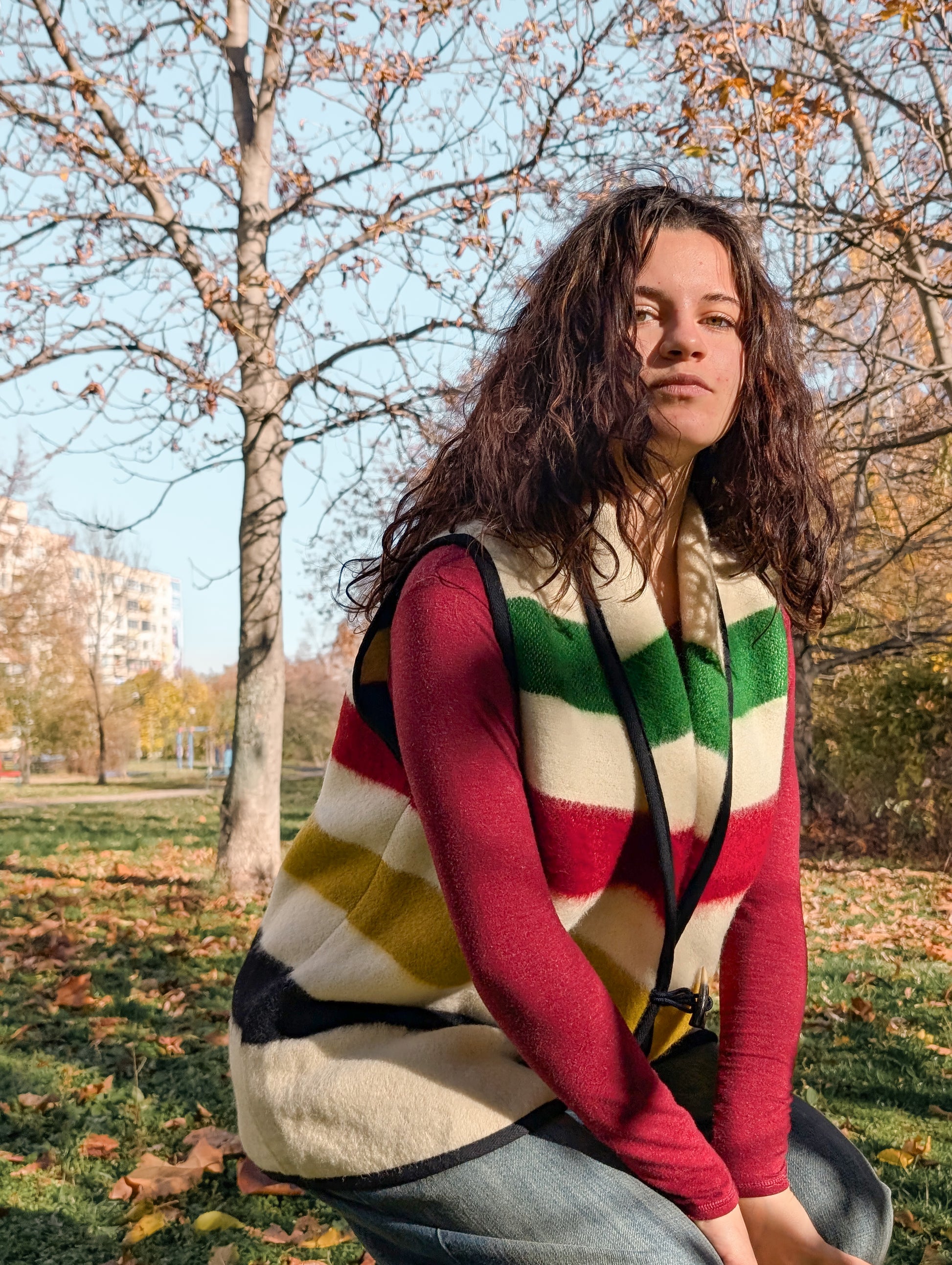Person wearing a beige sleeveless jacket vest with multicolor stripes, upcycled from authentic natural sheep wool blanket.