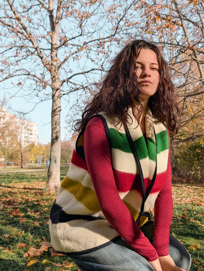 Person wearing a beige sleeveless jacket vest with multicolor stripes, upcycled from authentic natural sheep wool blanket.