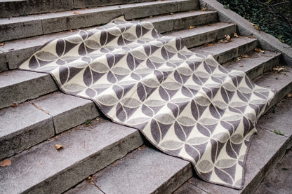 Luxurious geometric minimalistic wool blanket with circle pattern on stone steps, handwoven from sustainable undyed wool. 