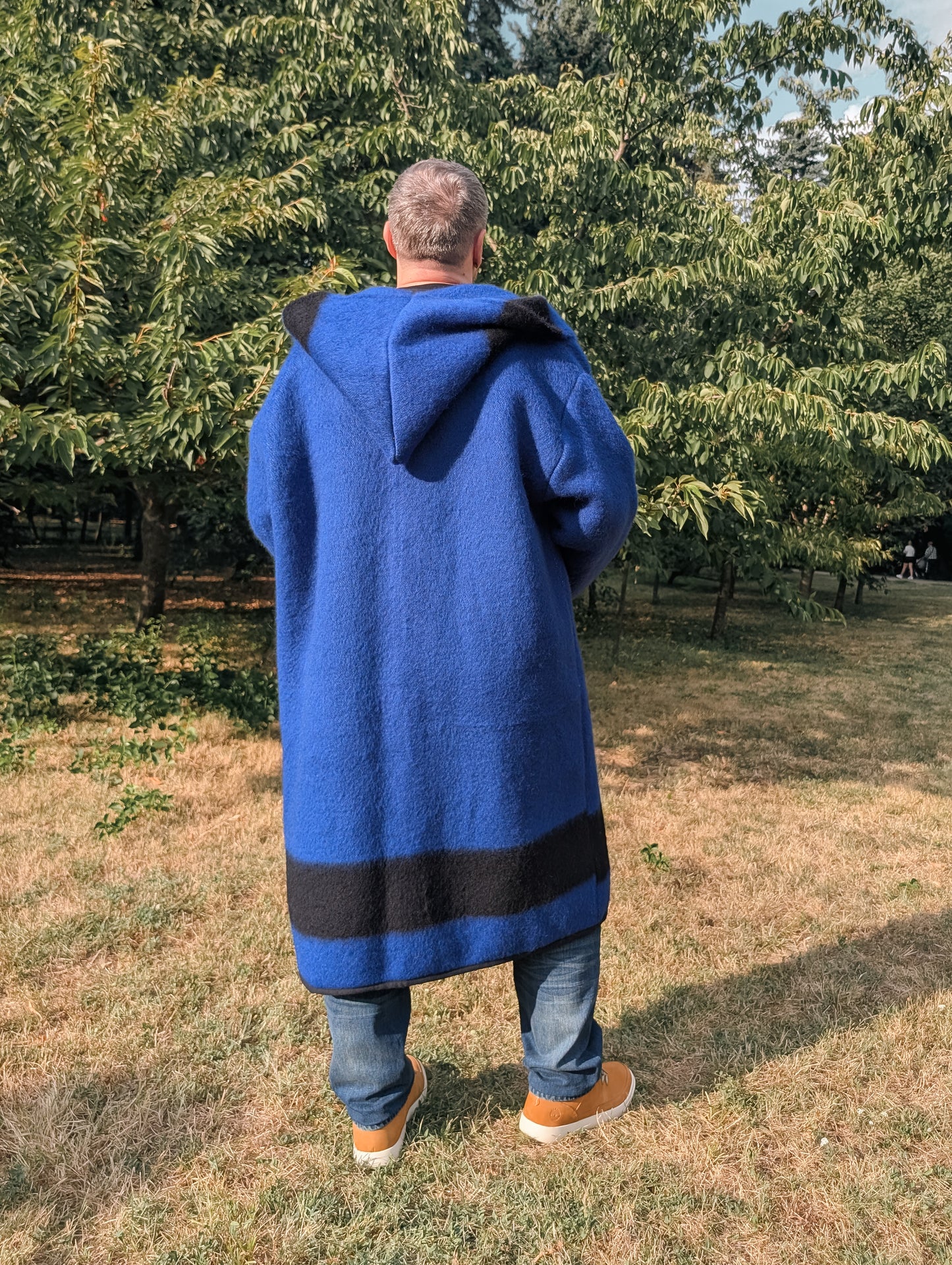 Person wearing a unisex overcoat, a hooded model, repurposed from a new traditionally woven blue blanket with stripes.