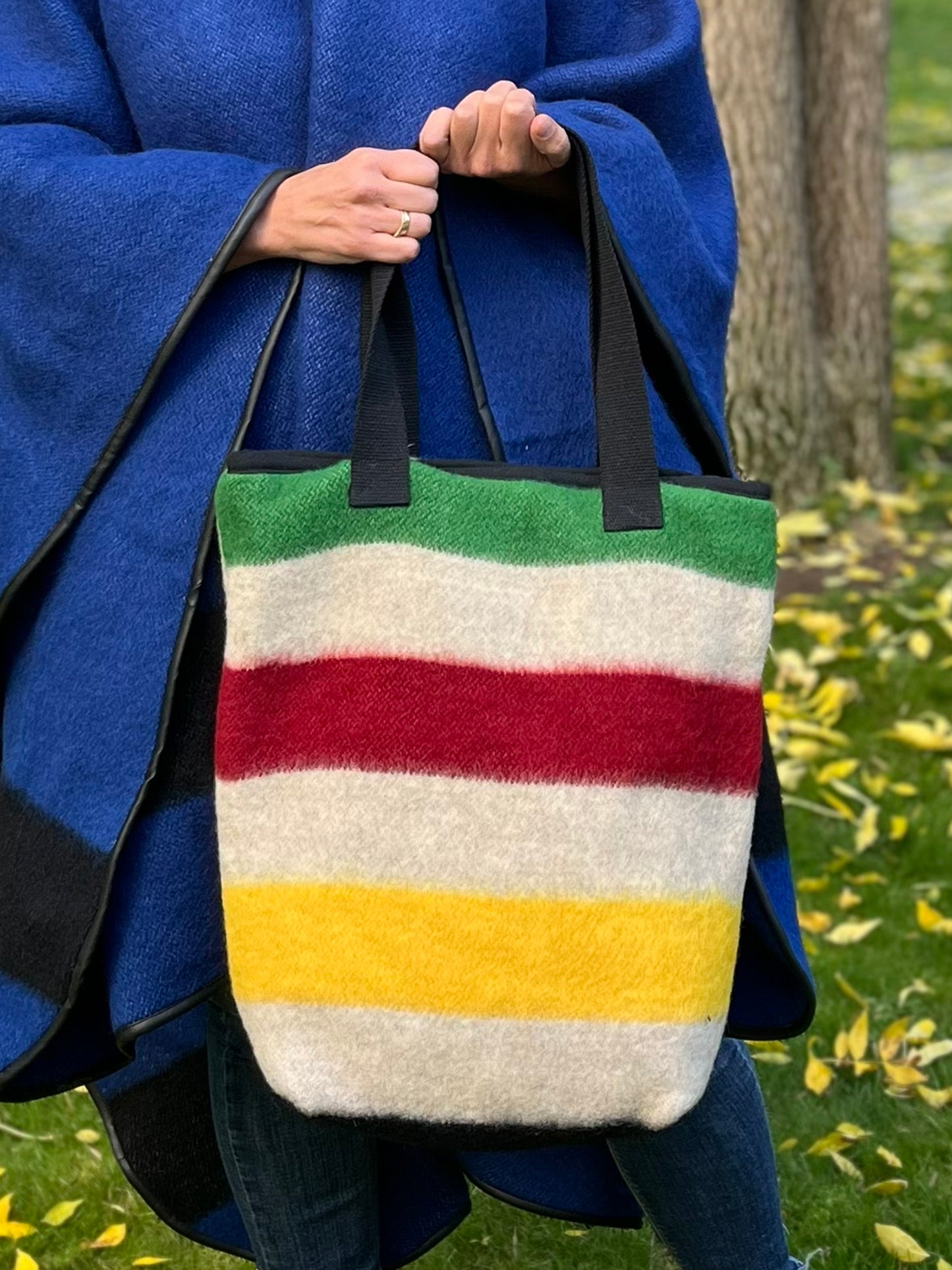Person holding a modern everyday tote bag in oatmeal gray base with colorful frontier stripes. This is a bespoke family studio product made from luxurious wool blanket cuts.