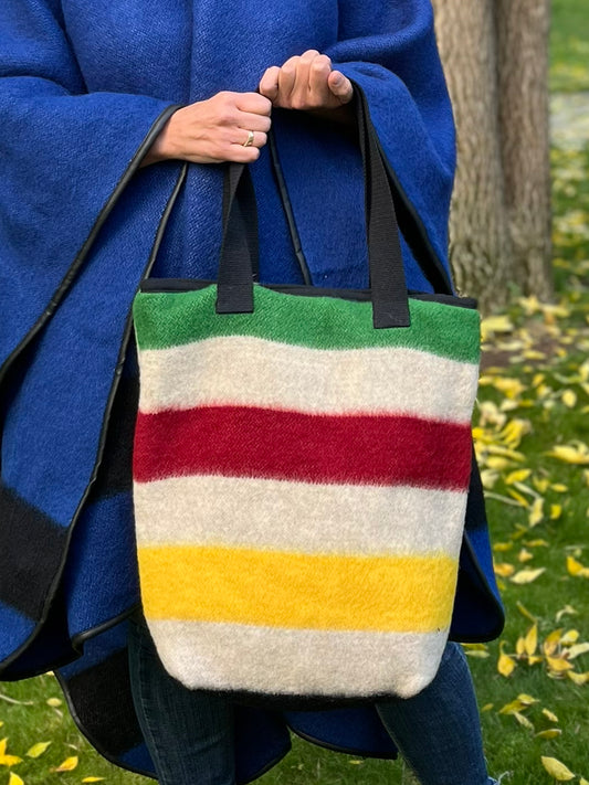 Person holding a modern everyday tote bag in oatmeal gray base with colorful frontier stripes. This is a bespoke family studio product made from luxurious wool blanket cuts.