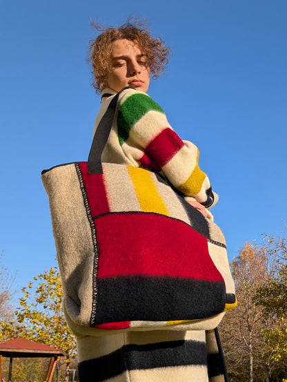 A young man wearing a large designer patchwork tote bag on his shoulder, matching his upcycled stripe duster coat. 