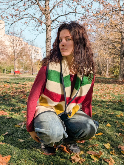 Woman with a multistriped wool blanket vest in cream base, with toggle closure. Unisex garment suitable for all occasions.