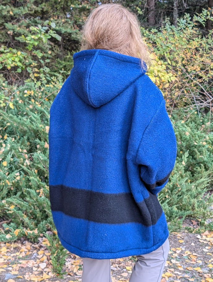 A woman posing bakwards and wearing a blue hooded anorak or boreal shirt, ideal for mountain camping, riverside walks and forest passages. The hoodie ismade of pure wool blanket.