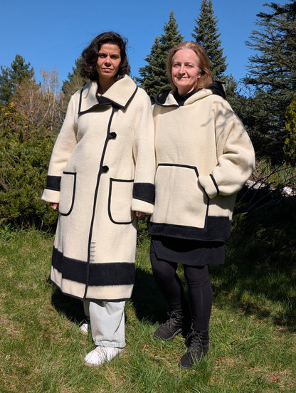 Two people wearing matching cream-colored coats with black stripes, made from single handwoven eco natural woolen blankets. 