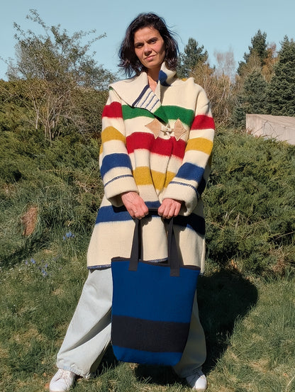 Woman wearing a midi striped coat with a hood, and holding a matching bag,  both upcycled from woolen blanket.