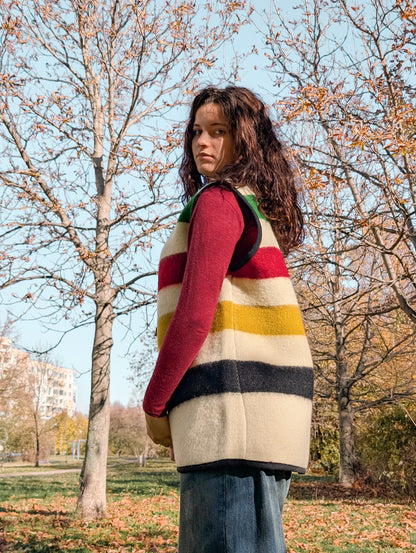 Young person wearing a unisex wool vest or sleeveless jacket in ivory base with colorful stripes, ideal for statement wear, streetwear, everyday style or statement slow fashion.