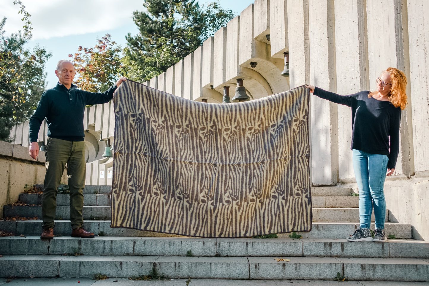 Two people holding a handwoven tribal wool blanket with ethnic safari motifs, made of natural wool.