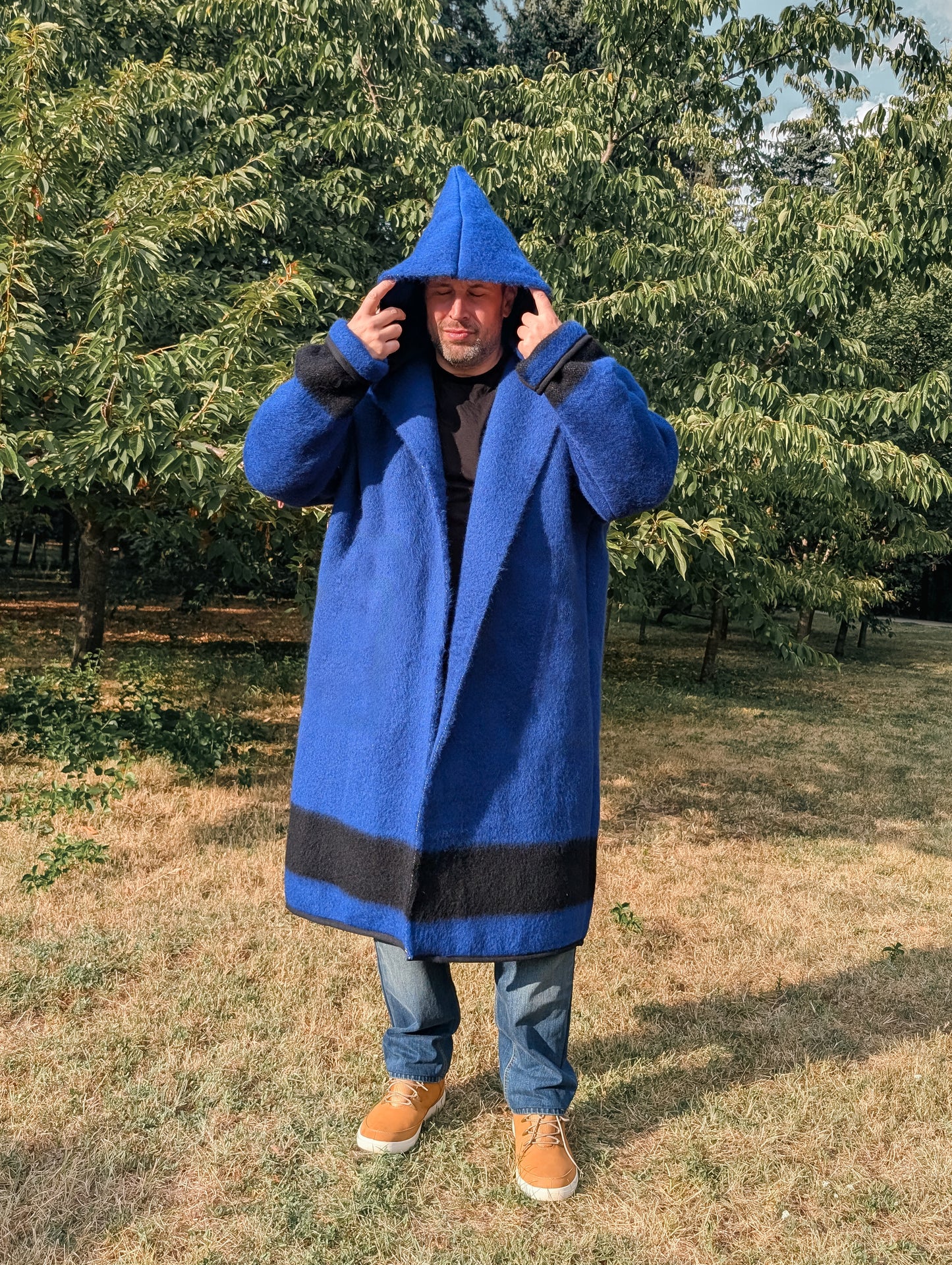 Man wearing long blue upcycled wool blanket capote coat, with a generous hood, made from iconic wool blanket in blue with a black stripe.