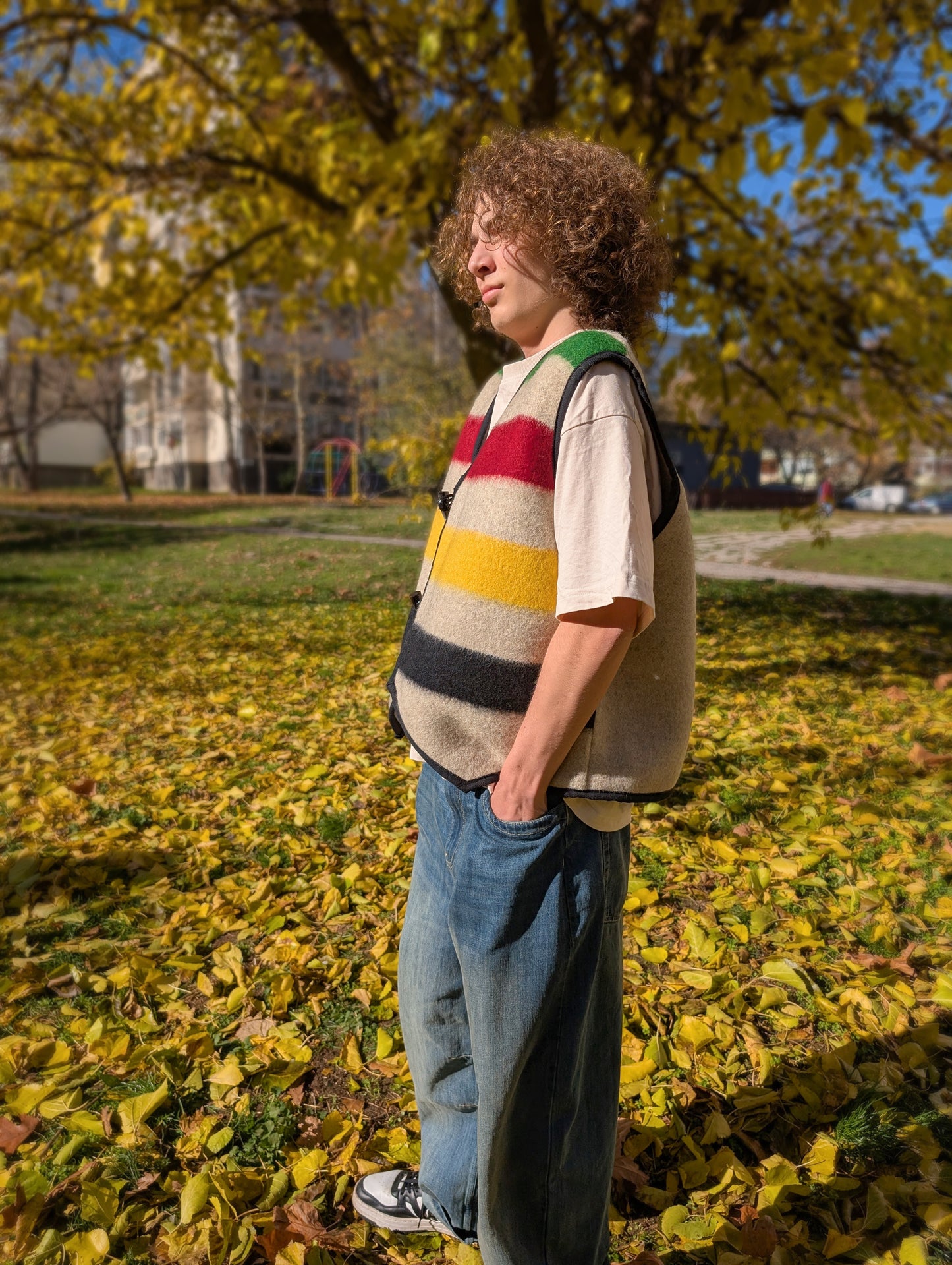 Young man stading in the park, wearing a cool stripe vest, great for street wear, everyday styling and walks in the nature.