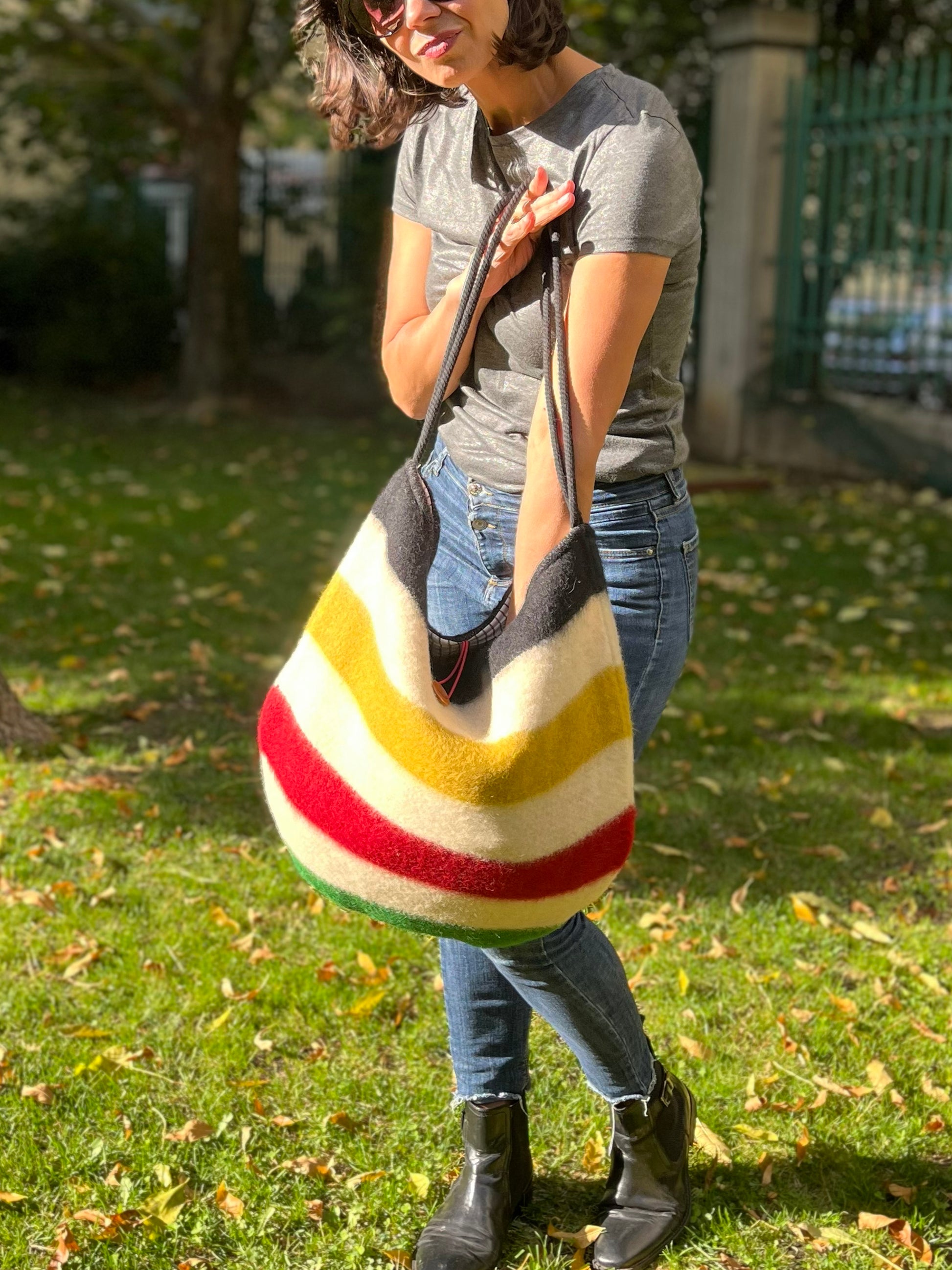Woman holding a modern everyday boho bag with iconic statement stripes in various colors. The bag is recycled from a luxurious authentic handwoven wool blanket. 