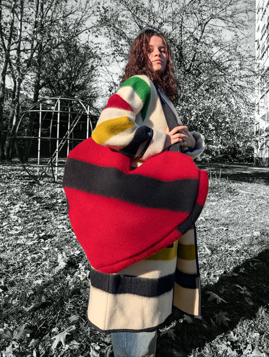 Young woman holding a large red heart-shaped shoulder bag in an outdoor setting with trees and playground equipment.