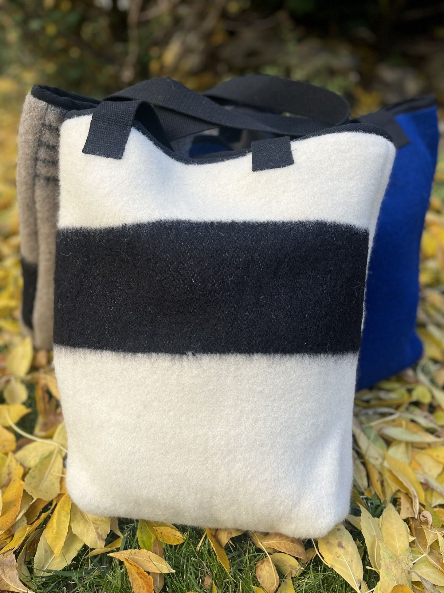 A large ivory wool blanket tote bag with a signature single black stripe in front. 