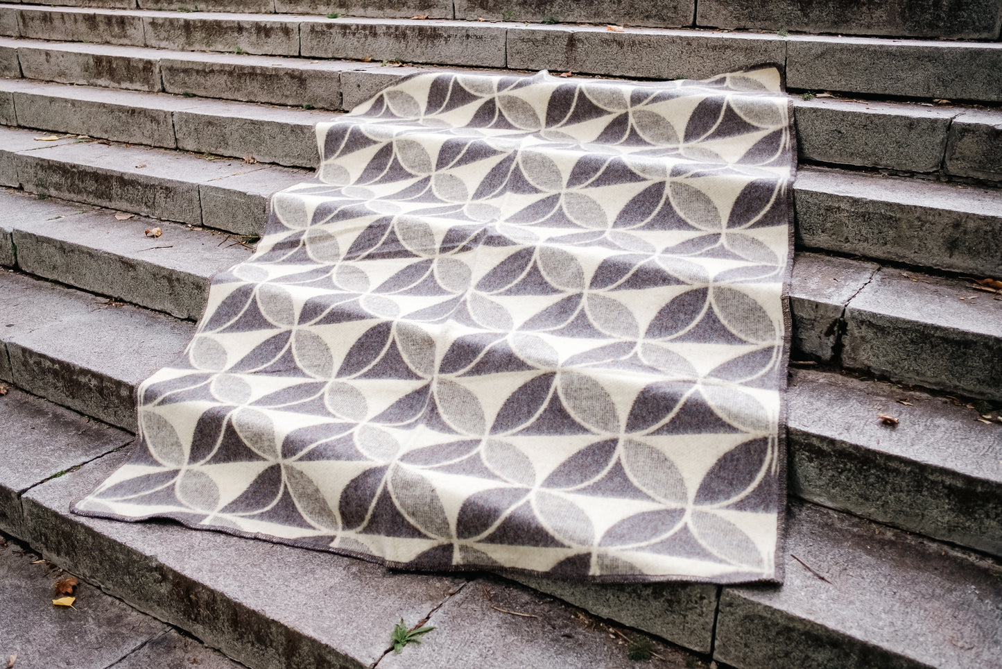 Cozy minimalistic blanket with geometric circles pattern, handwoven from undyed virgin sheep wool, spread on stone steps