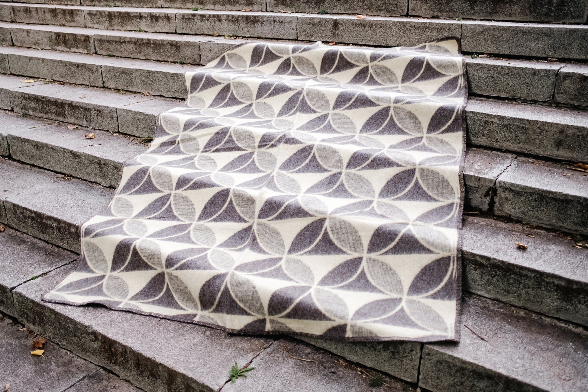 Cozy minimalistic blanket with geometric circles pattern, handwoven from undyed virgin sheep wool, spread on stone steps