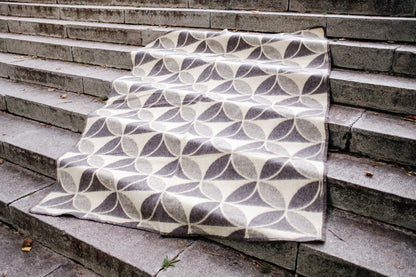 Cozy minimalistic blanket with geometric circles pattern, handwoven from undyed virgin sheep wool, spread on stone steps