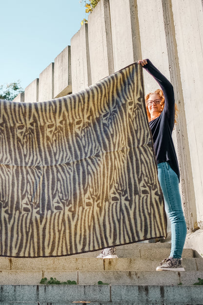 Person holding a thick wool natural dyed blanket with ethnic safari and tribal folk or native motifs resembling zebra patterns