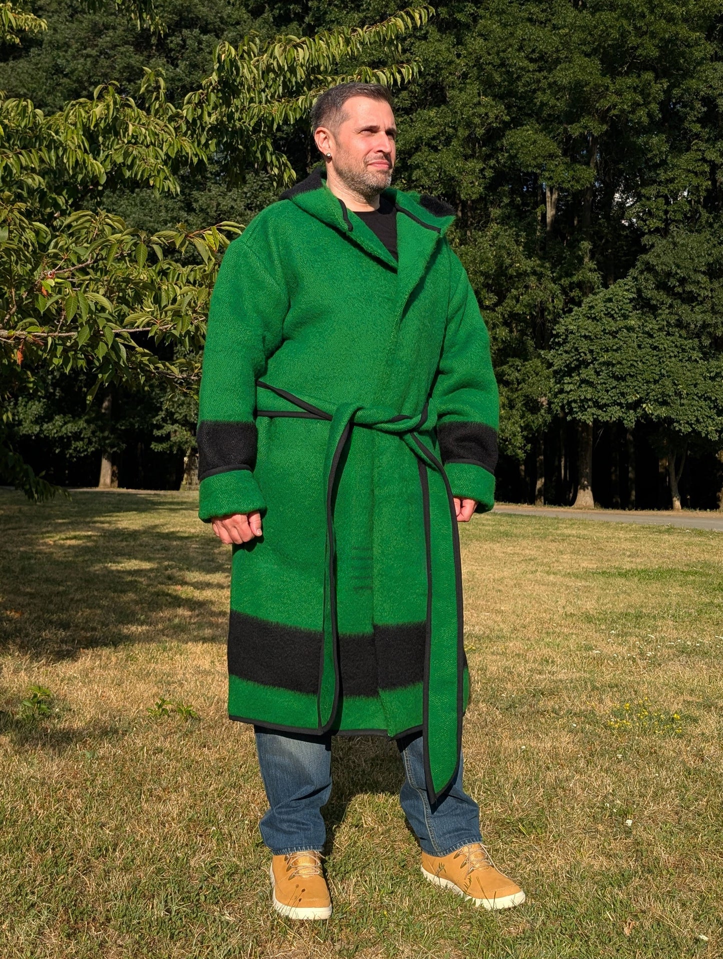 Man wearing a green wool robe coat with matching fabric belt and a wide hood. This piece is upcycled from a traditionally woven wool blanket.