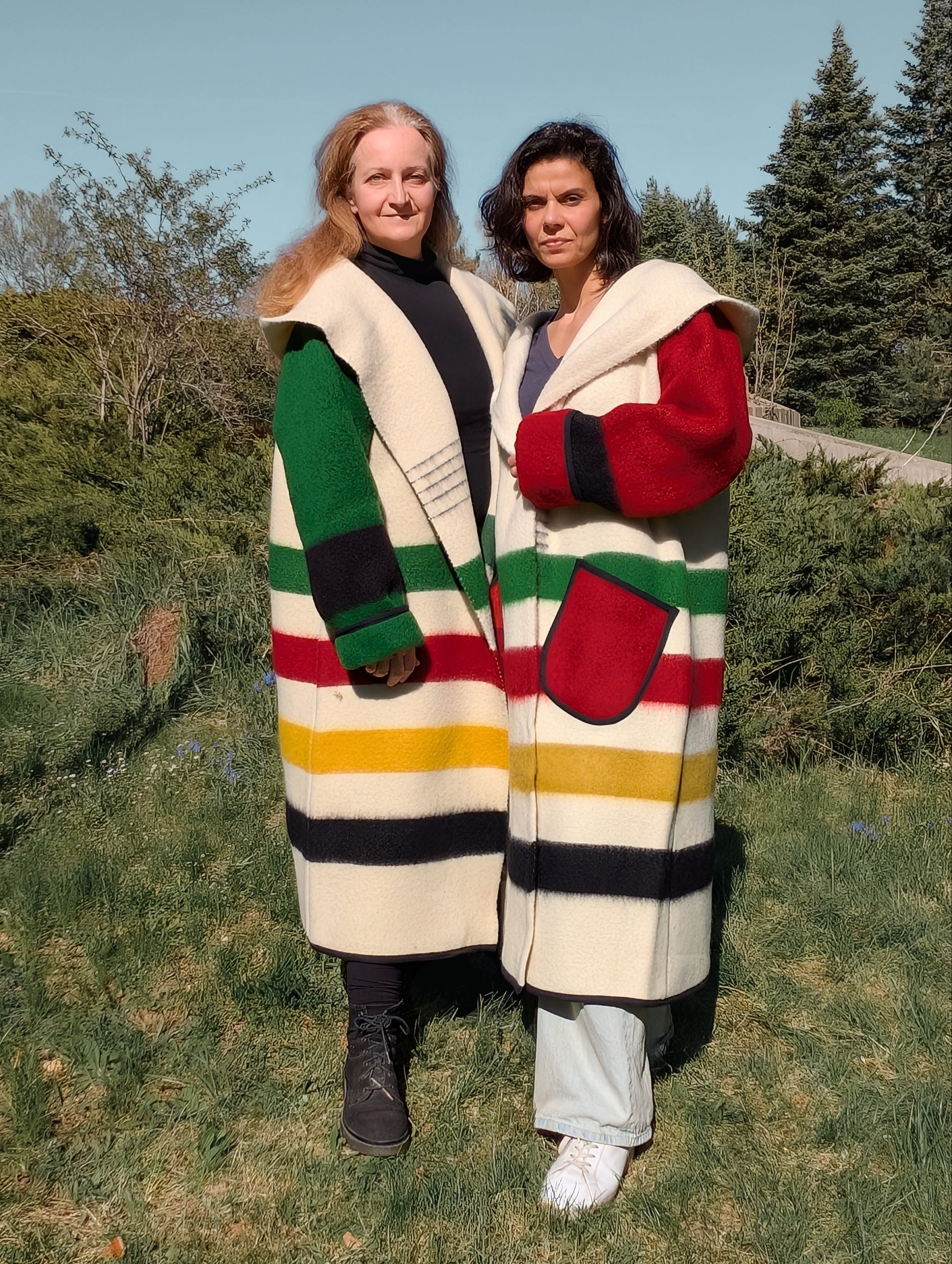 Two women wearing oversized unisex blanket overcoats with stripes distinctive colorful sleeves.