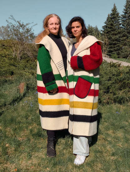 Two women wearing oversized unisex blanket overcoats with stripes distinctive colorful sleeves.