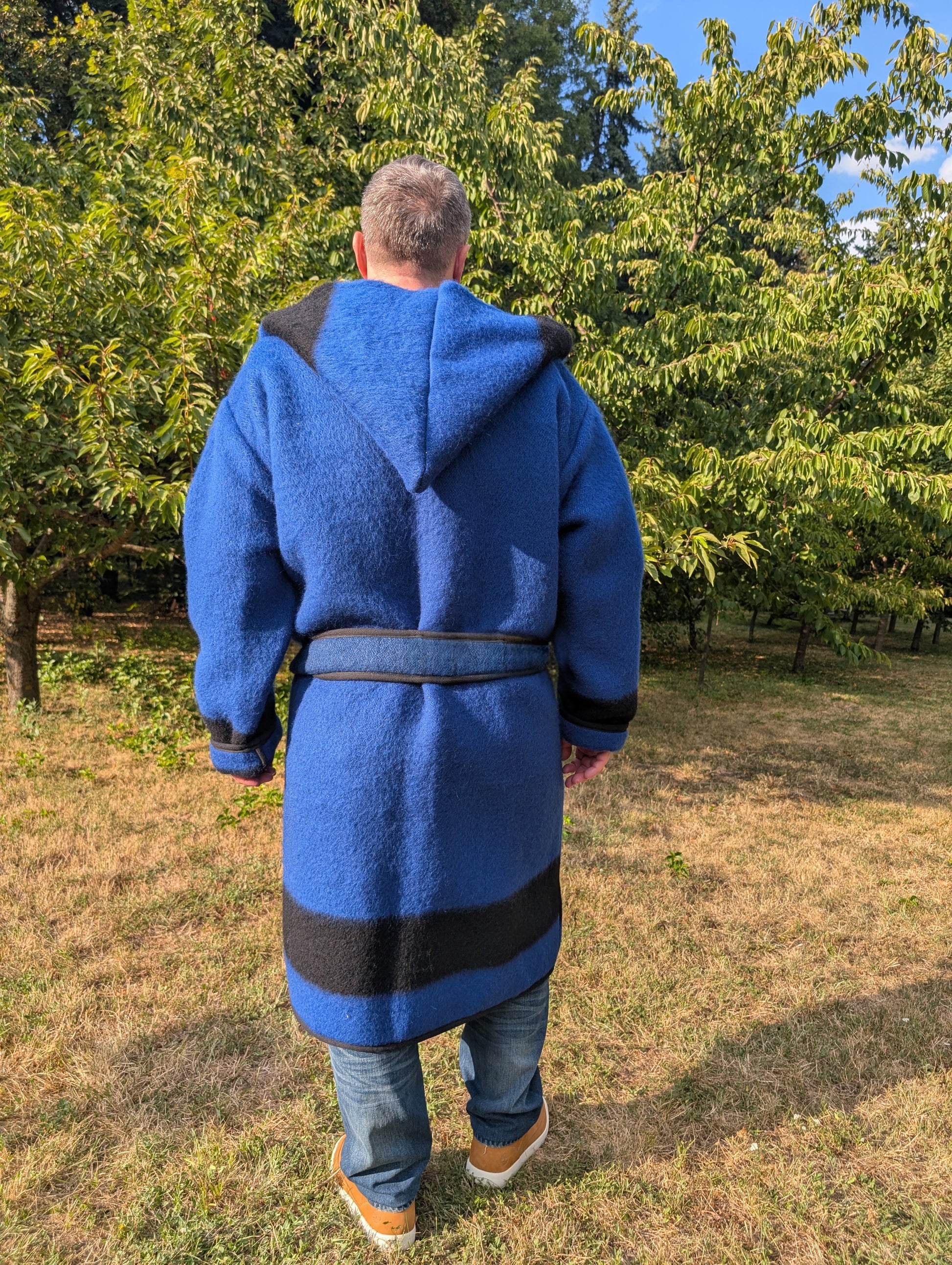 Person wearing a beautiful warm made-to-order capote coat, wrapped with a belt, with a old fashion large hood. Both a comfortable and impressive outerwear.