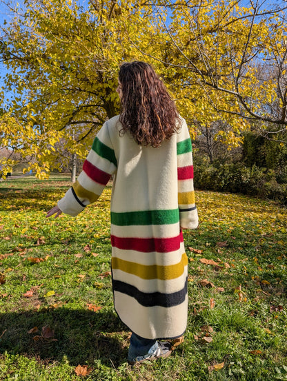 A girl standing backwards and wearing oversized duster coat with stand collar, upcycled from a pure virgin natural wool classic multistripe blanket. 