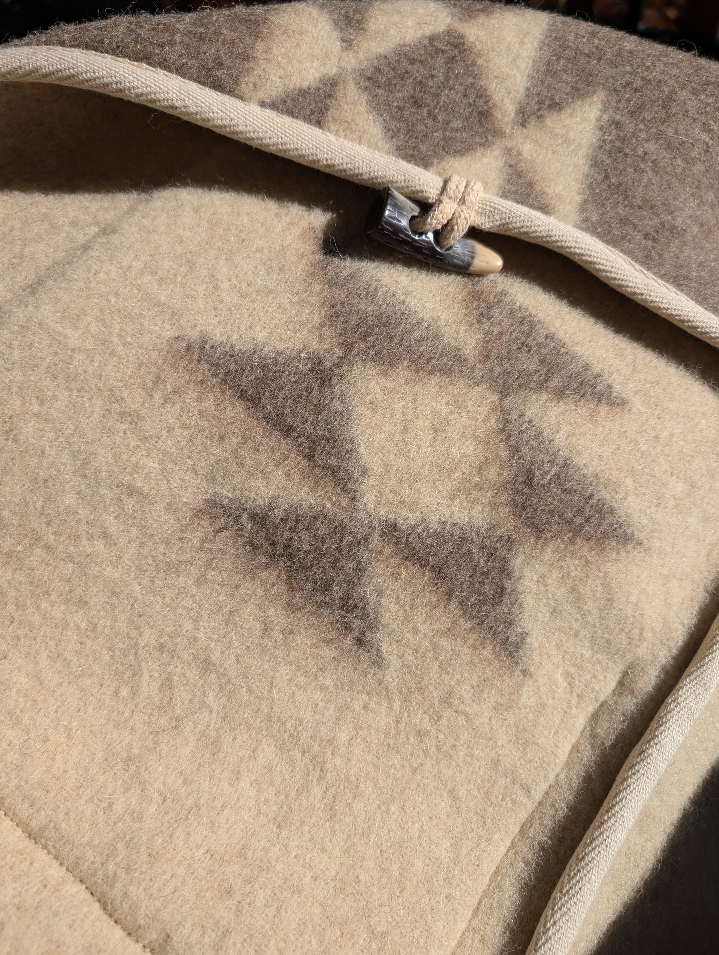A closeup of a Robe Coat upcycled from undyed virgin wool blanket with indian diamond patterns, and a toggle closure.