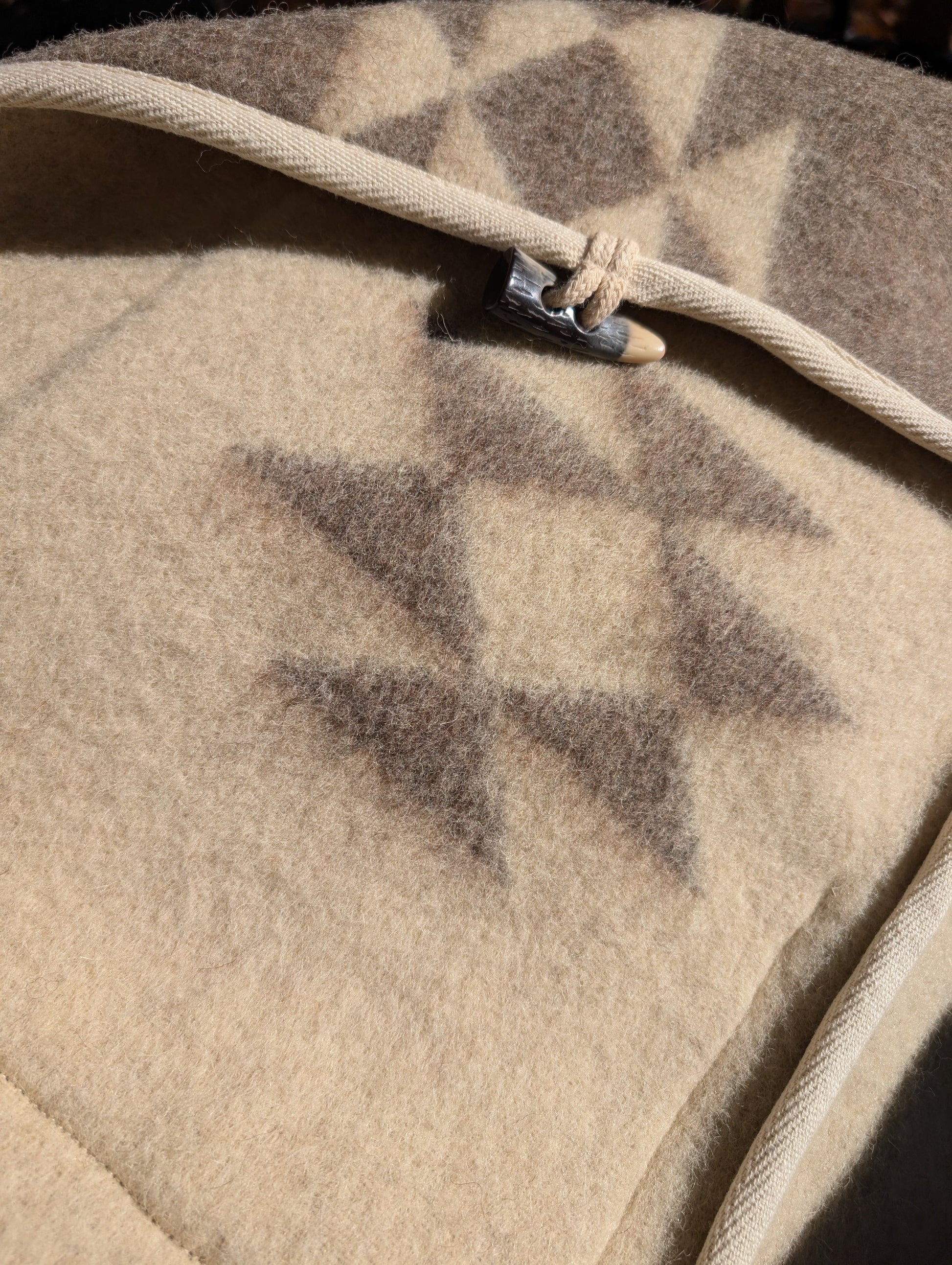 A closeup of a Robe Coat upcycled from undyed virgin wool blanket with indian diamond patterns, and a toggle closure.