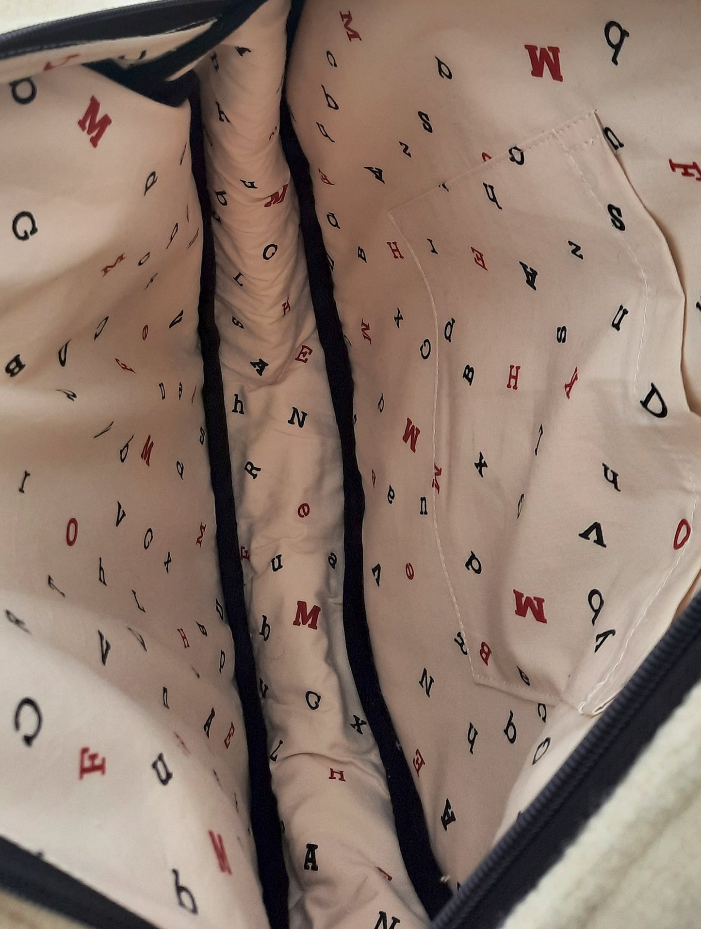 Close-up of a tote bag interior lining with letter patterns on a beige background.