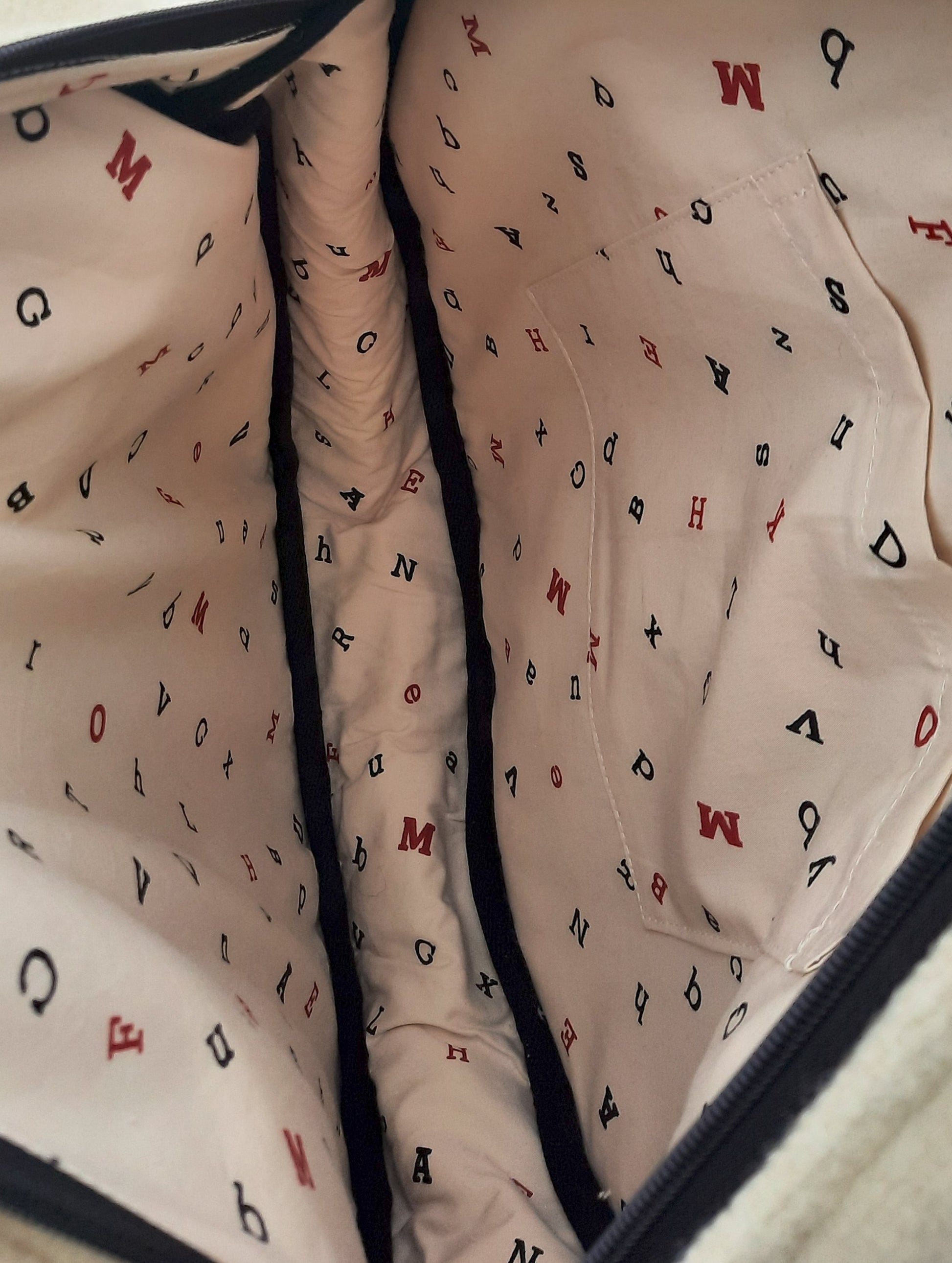Close-up of a tote bag interior lining with letter patterns on a beige background.