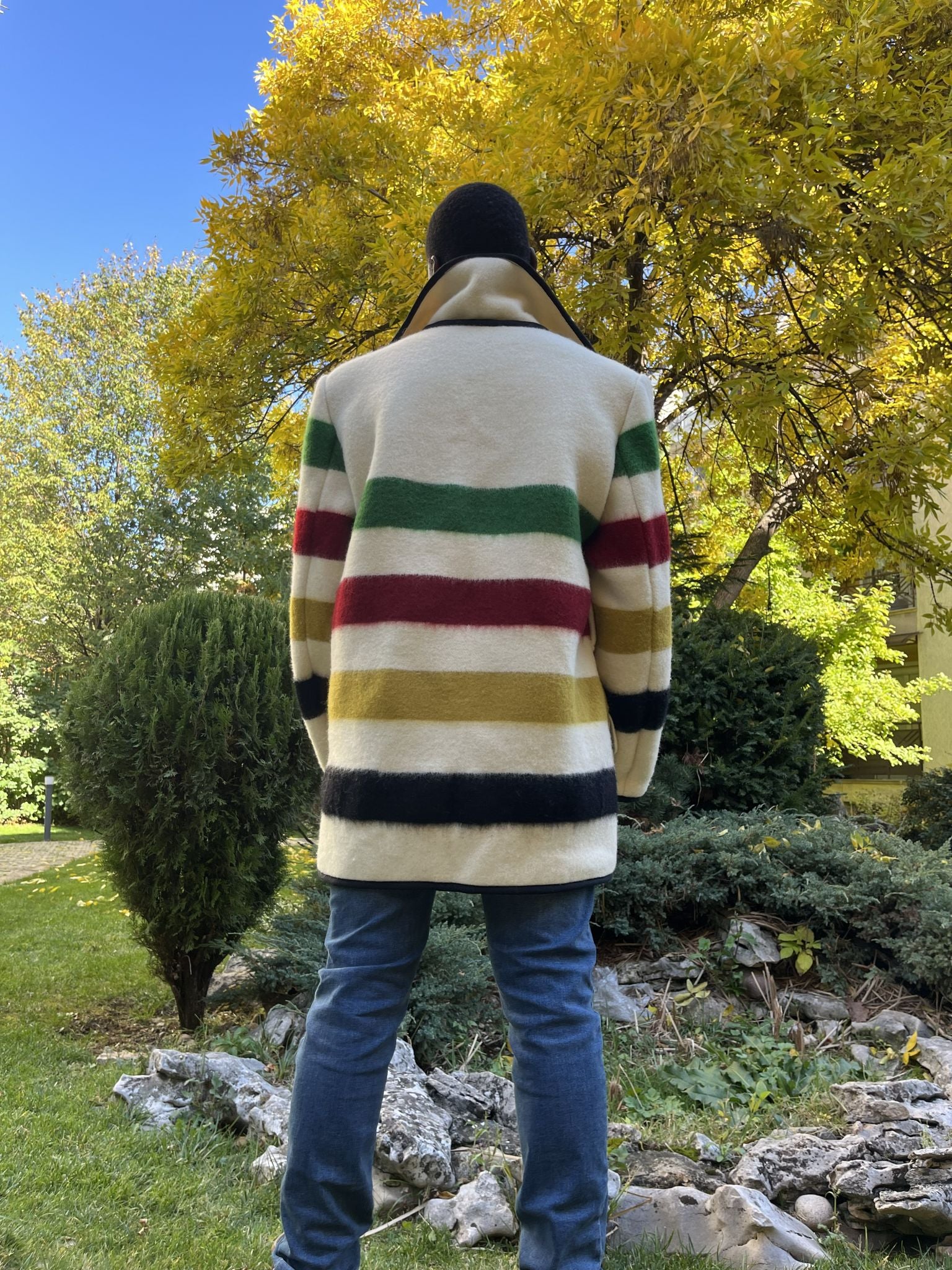 Person posing backwards and wearing a stylish 1970s blanket trench coatupcycled from a pure wool heritage striped blanket.