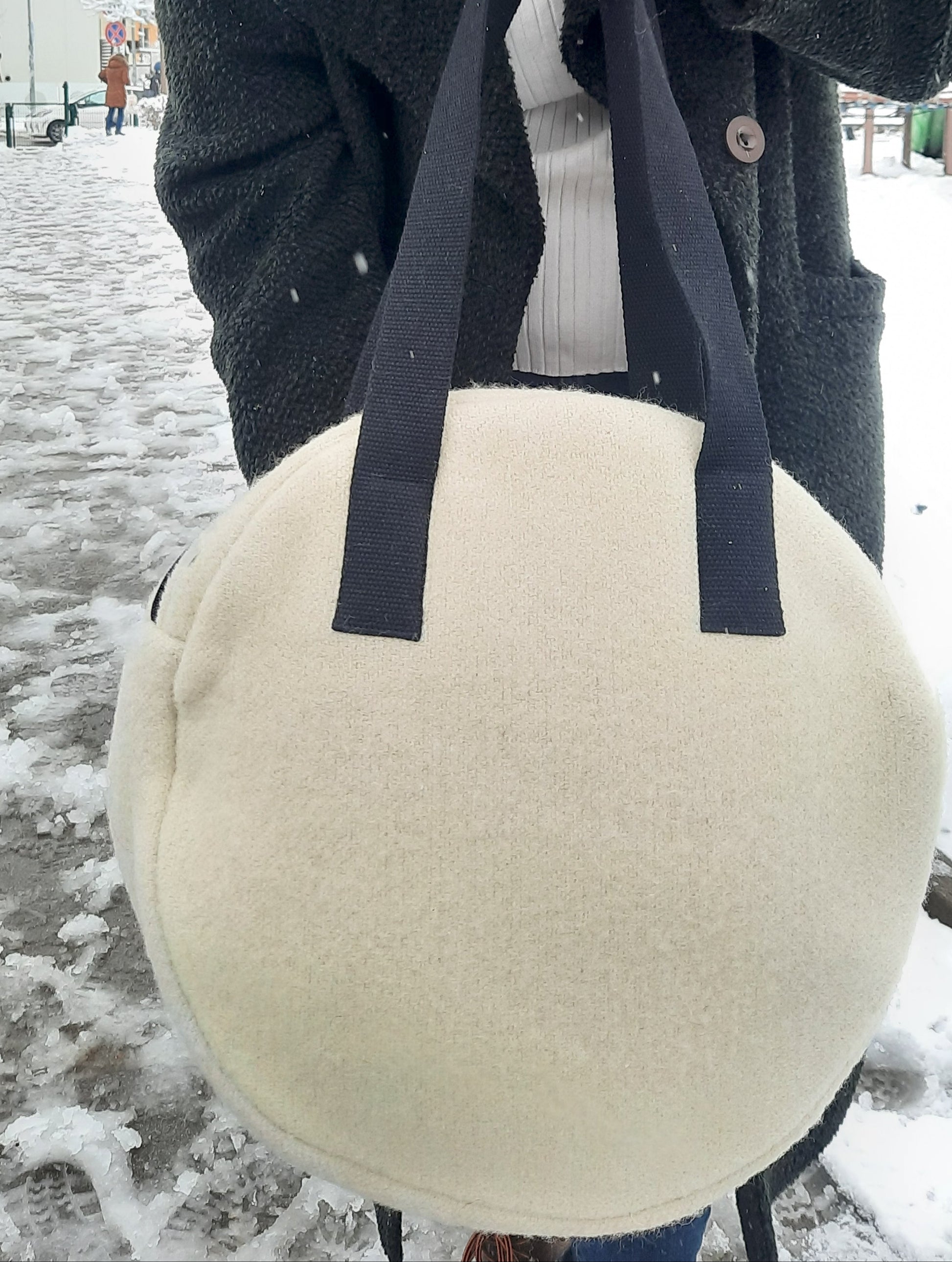 PLain backside of an upcycled wool blanket round tote bag with black straps held by a person in an urban setting