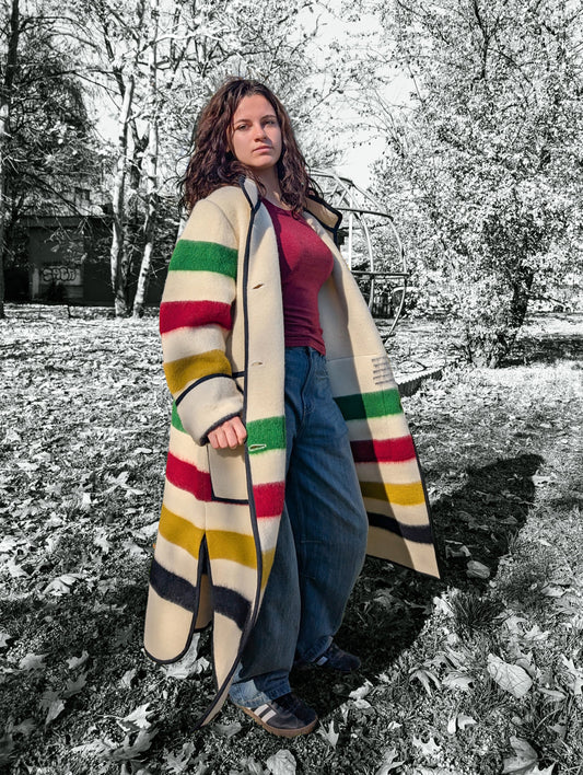 A girl wearing a fashionable long oversized duster coat with stand collar, two front pockets and single breasted, upcycled from a pure virgin natural wool classic multistripe blanket. 