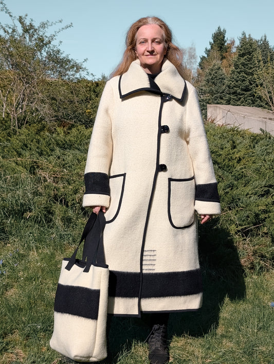 Woman wearing a long woolen overcoat and a matching hand bag, both upcycled from a handmade traditional sustainable blanket.