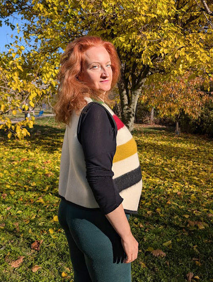 Woman wearing a luxurious upcycled blanket giled or vest with colorful stripes at the front and plain back. A classic cowboy model with a V-front and toggle closure.