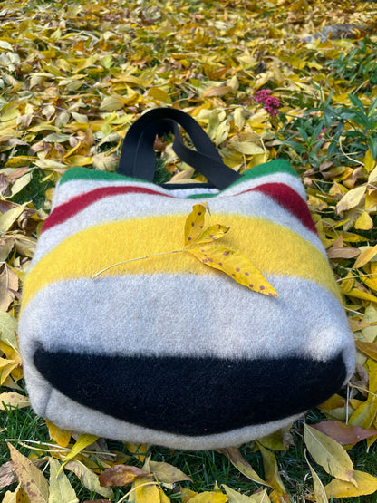 Upcycled tote bag made from locally handmade stripe wool blanket cuts with multicolor stripes, on a leaf-covered ground