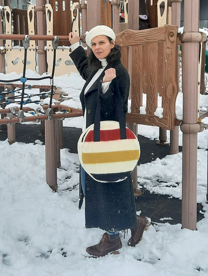 Woman standing in a snowy playground holding a modern colorful circle bag suitable for every day and street wear.