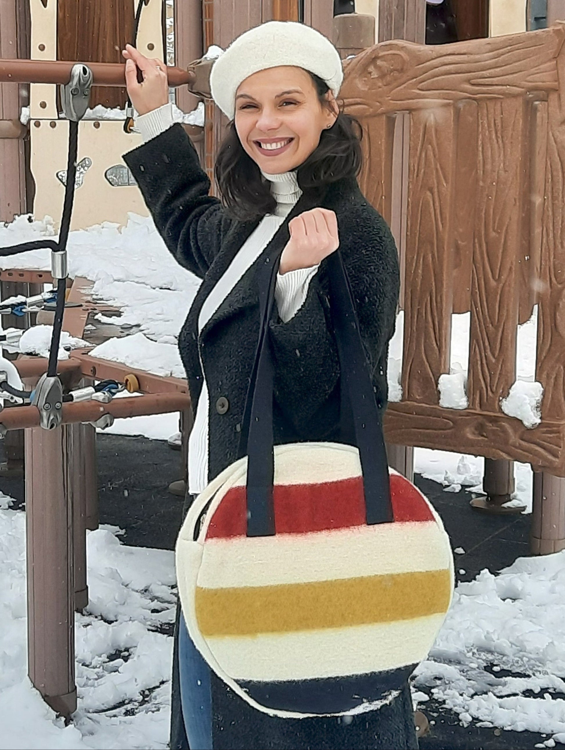 Woman holding a multistripe round tote bag with black straps. Handmade upcycled from pure wool frontier blanket.